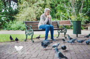 Una mujer sentada en un banco con palomas a su alrededor