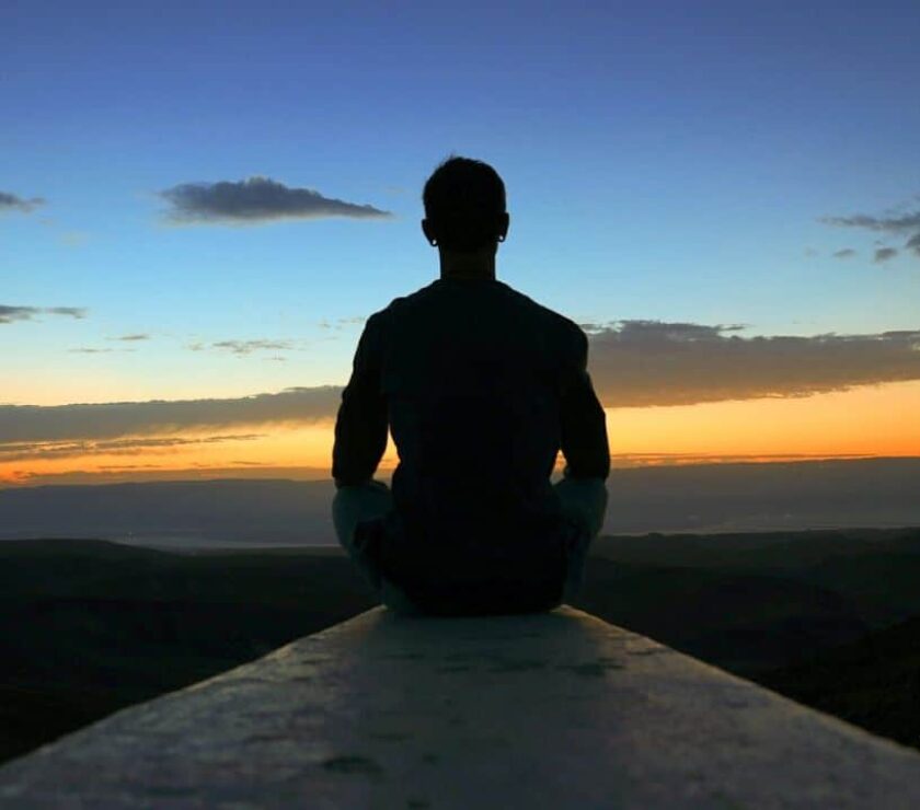 Hombre sentado frente a una puesta de sol sintiendo los cambios transformadores del mindfulness
