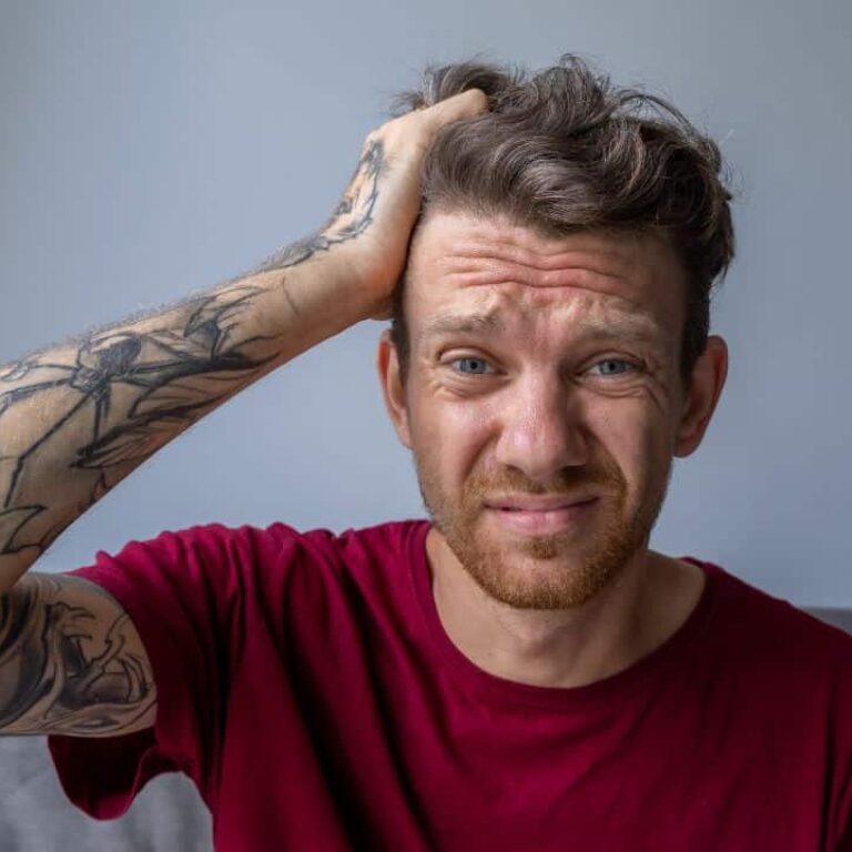 Un hombre con camiseta roja y tatuajes en el brazo llevándose la mano a la cabeza por un diagnóstico tardío de tdah en adultos