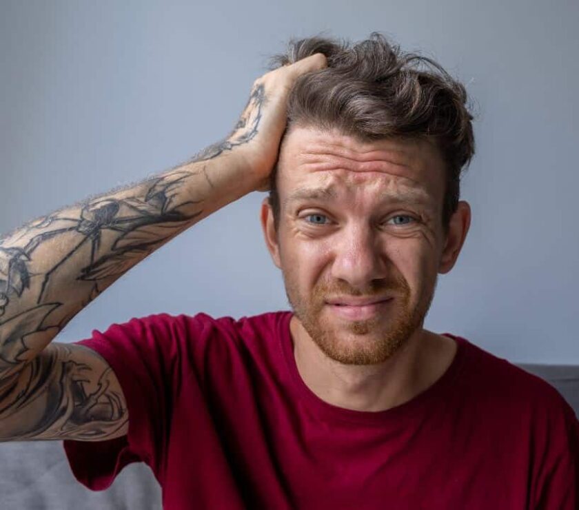 Un hombre con camiseta roja y tatuajes en el brazo llevándose la mano a la cabeza por un diagnóstico tardío de tdah en adultos