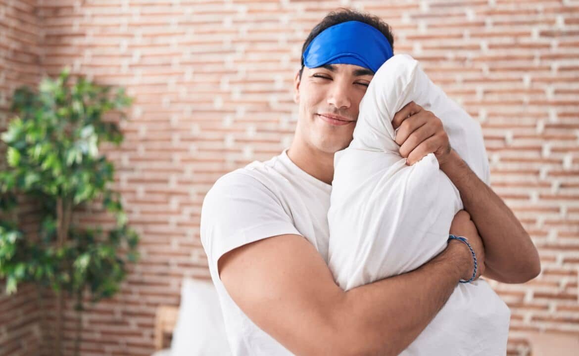 joven con antifaz y somnoliento abrazando una almohada para dormir mejor