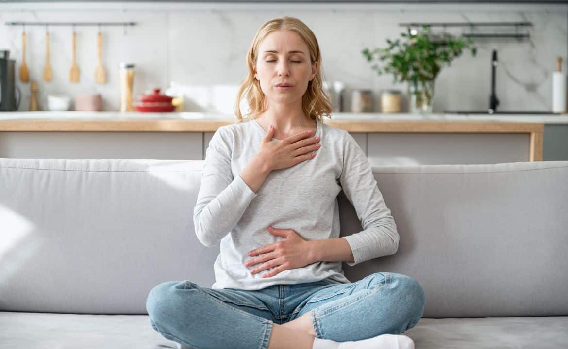 Mujer sentada en sofá concentrada practicando técnicas de respiración para la ansiedad