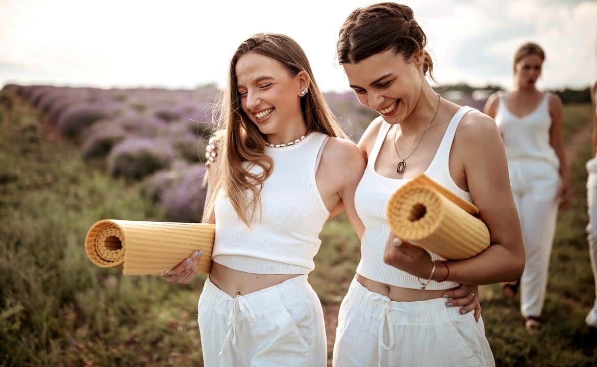 Dos mujeres sonriendo caminando juntas con esterillas de yoga notando los beneficios del yoga y salud mental