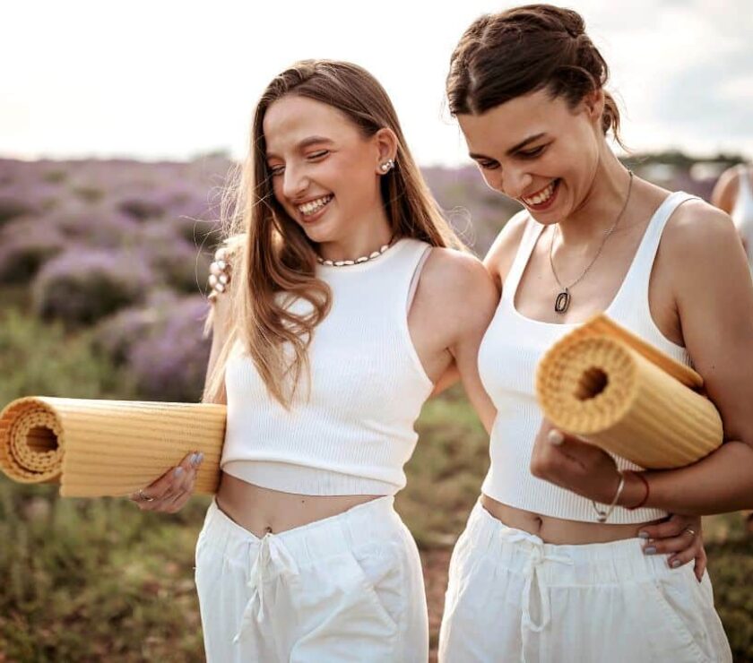 Dos mujeres sonriendo caminando juntas con esterillas de yoga notando los beneficios del yoga y salud mental