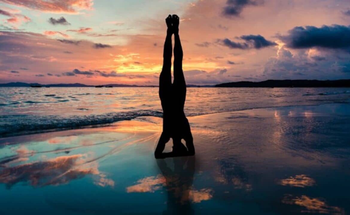 persona en la playa en postura sirsasana de yoga como expresión corporal
