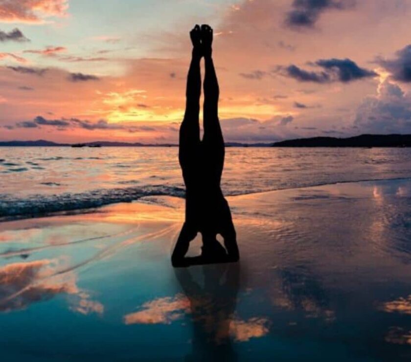 persona en la playa en postura sirsasana de yoga como expresión corporal