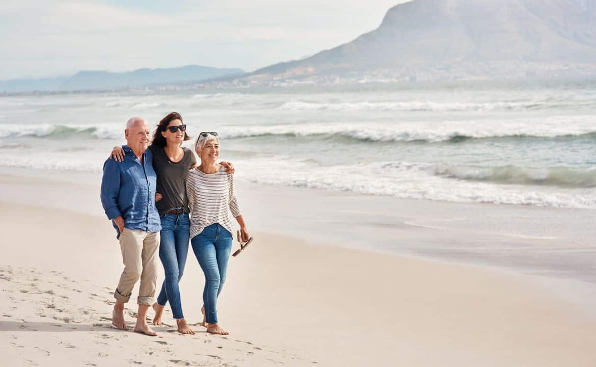 Tres personas caminando por la playa descalzos y abrazados disfrutando de la calidad de vida