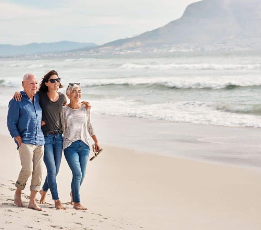 Tres personas caminando por la playa descalzos y abrazados disfrutando de la calidad de vida