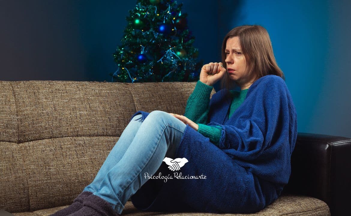 Mujer recogida en un sofá abrigada con una manta intentando manejar el estrés de las fiestas.