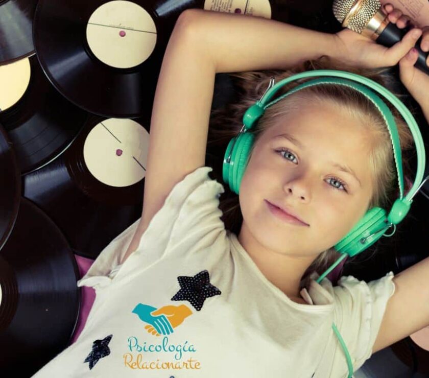 Niña con auriculares y micrófono recostada sobre un lecho de vinilos disfrutando de los beneficios de la música.