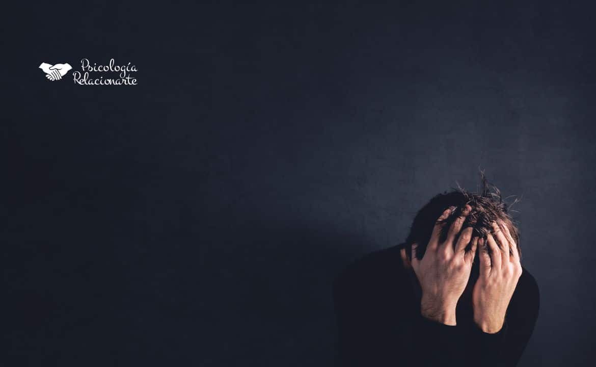 Hombre con jersey negro agachado con las manos en la cabeza viviendo la experiencia de pérdida y el duelo
