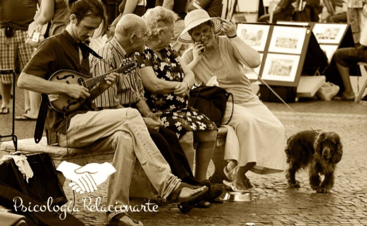 Grupo de gente conversando en un banco en la calle y un músico con una mandolina mejorando las relaciones con comunicación consciente.