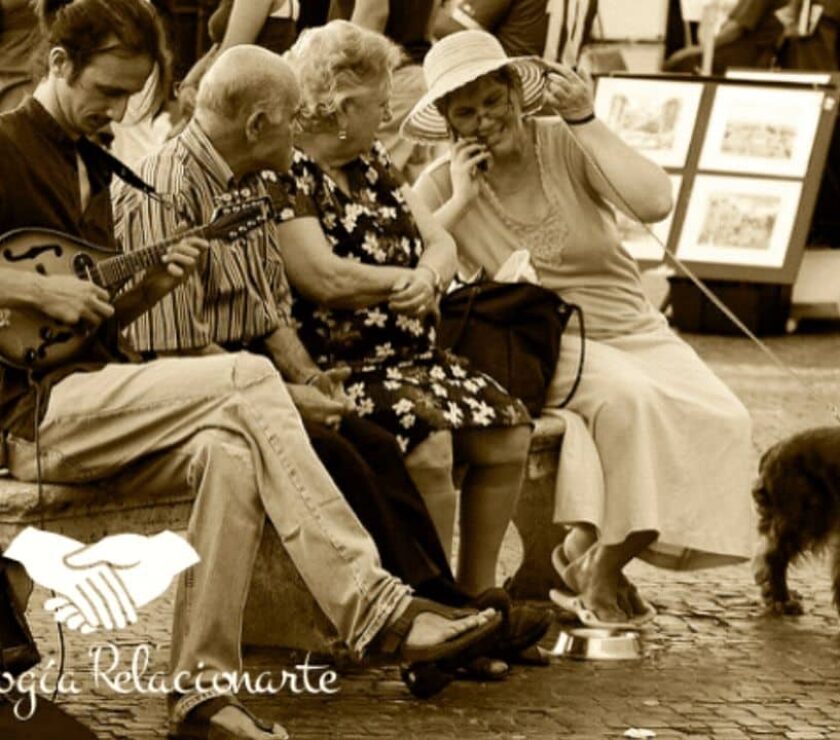 Grupo de gente conversando en un banco en la calle y un músico con una mandolina mejorando las relaciones con comunicación consciente.