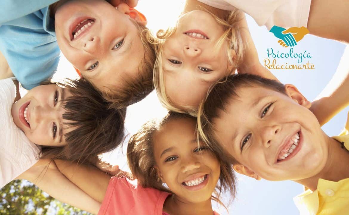 Grupo de niños con sus cabezas juntas formando un círculo sonriendo reflejando la relación entre infancia y amigos