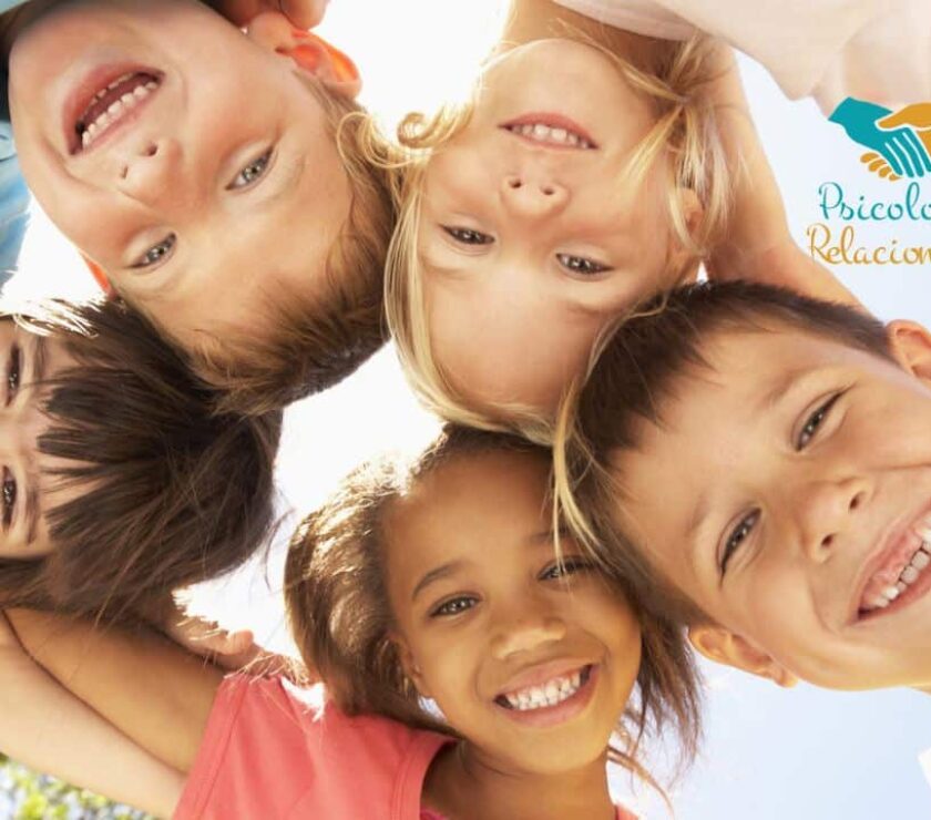 Grupo de niños con sus cabezas juntas formando un círculo sonriendo reflejando la relación entre infancia y amigos
